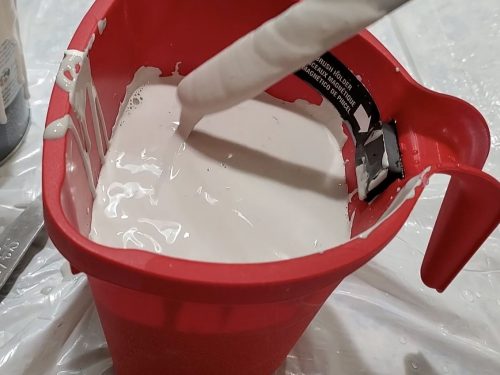 Mixing water and chalk paint inside a red bucket.