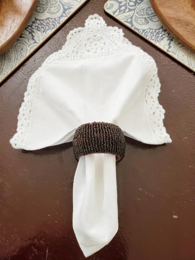 White antique cloth napkin inside a brown beaded napkin ring.