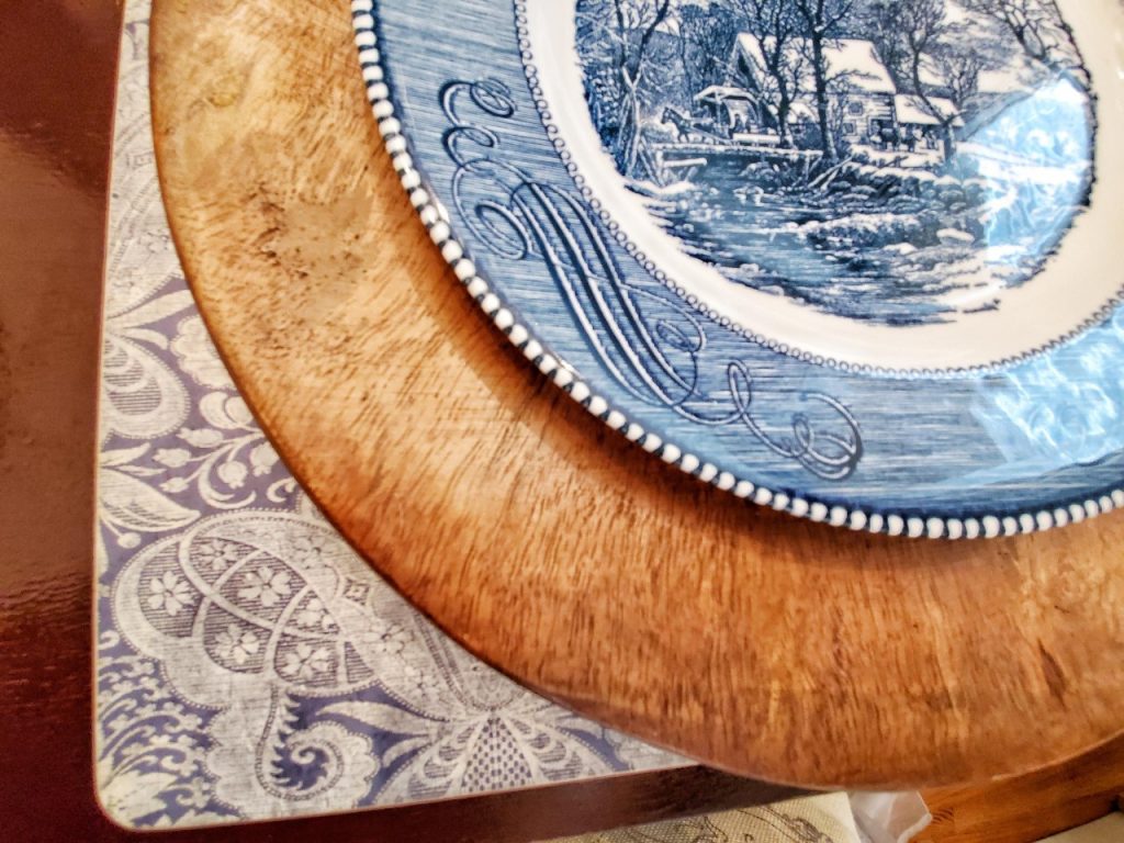 Up close photo of a blue damask placemat, wood charger and Currier and Ives dinner plate.