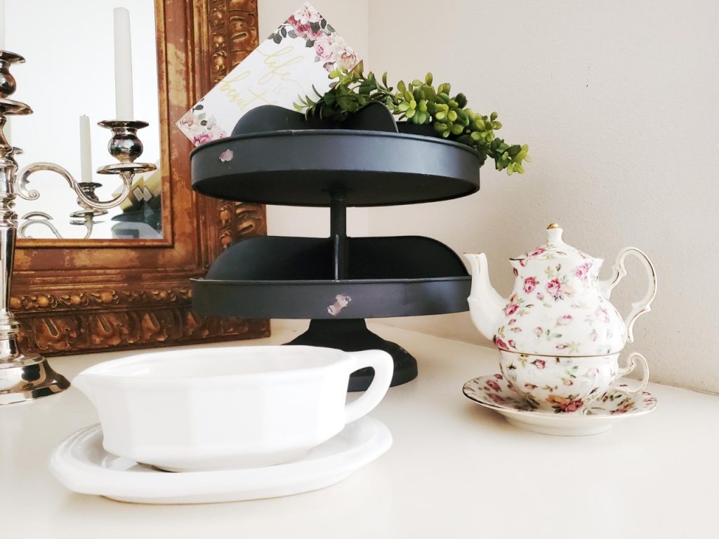 Black tiered tray. Pfalzgraff gravy bowl and plate. Teapot and teacup combo. All on top of a fireplace mantle.