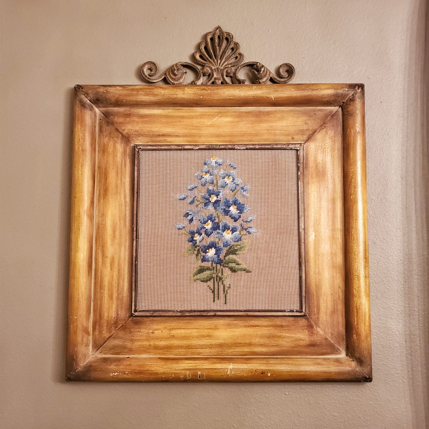 Metal frame that looks like wood. Blue floral embroidered piece inside frame. Found at a thrift store.