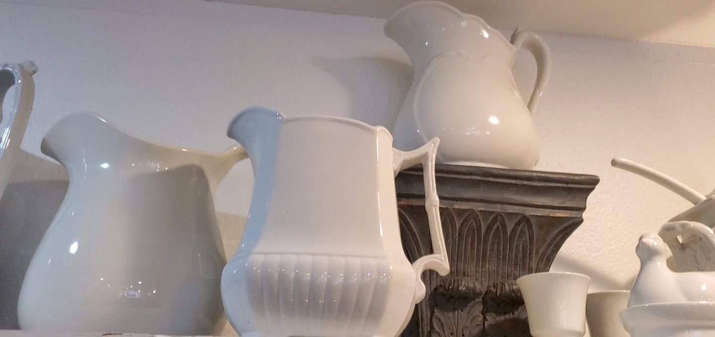 White ironstone pitchers on a shelf at an antique store.