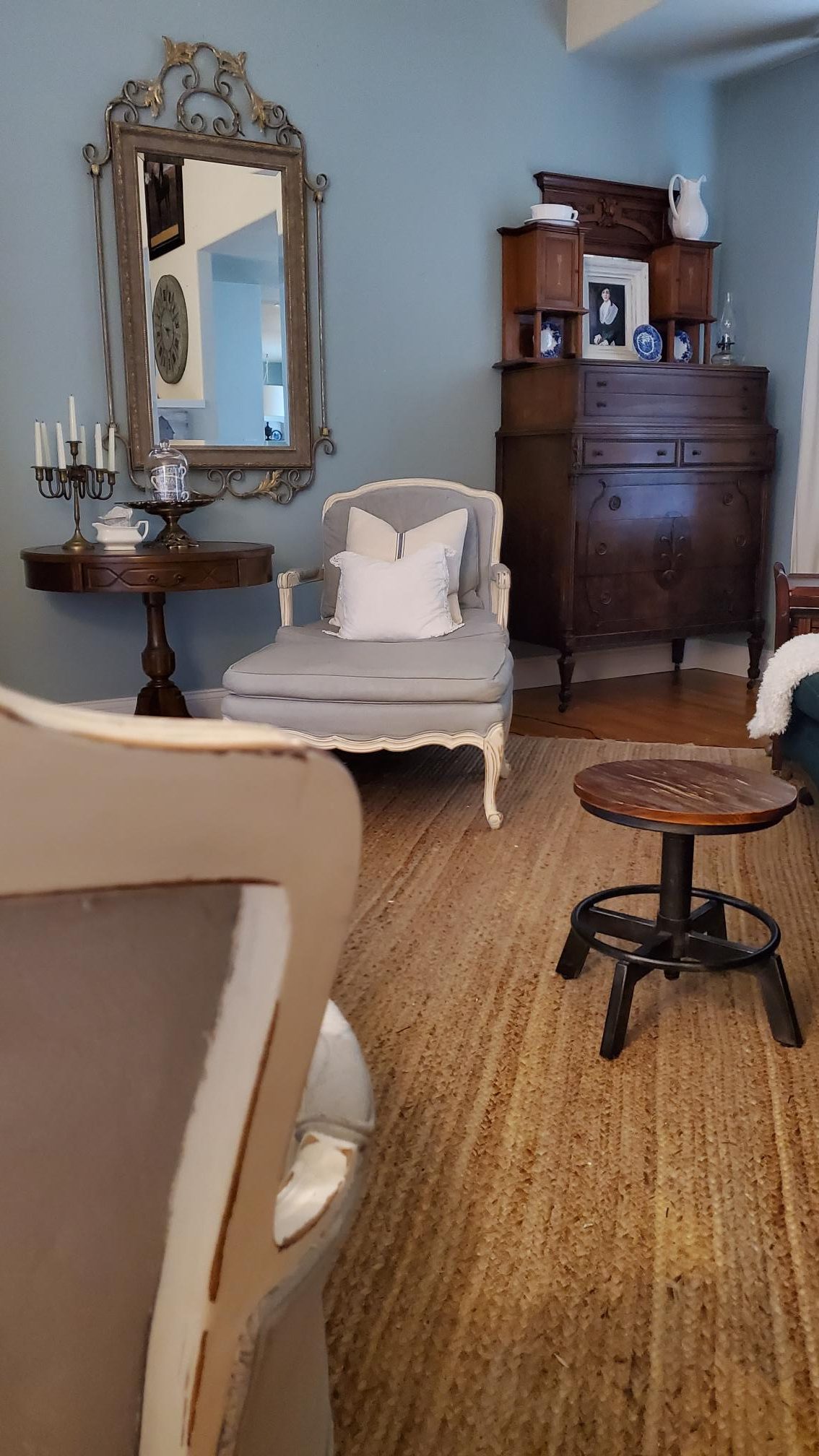 Living room with a chair and ottoman. Antique dresser and large gold and grey mirror.